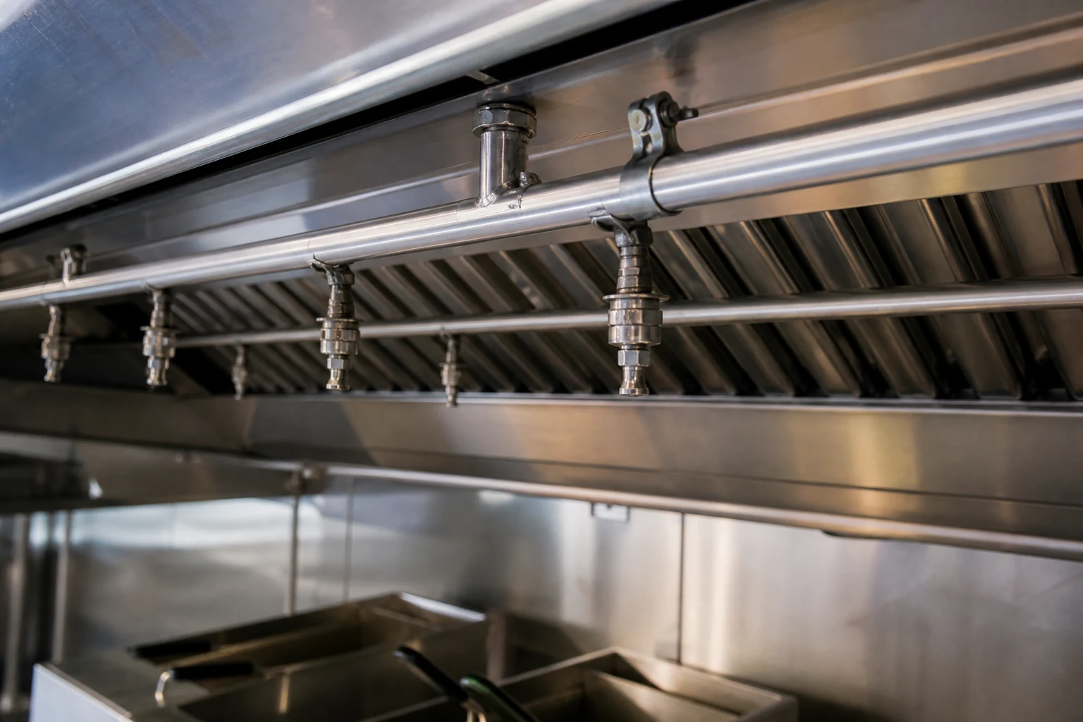 Kitchen fire suppression nozzles and piping installed beneath a commercial exhaust hood.
